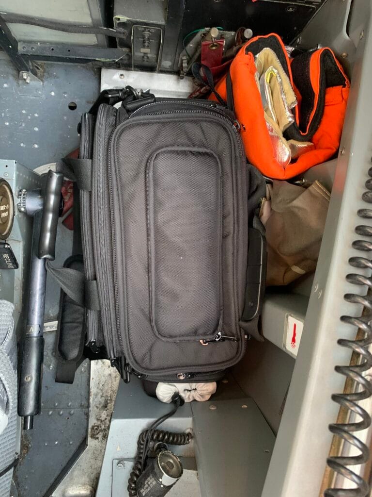 A top down view of the Aerocoast Pro Crew I bag beside the pilot seat in a B737 classic aircraft. The view also shows some of the aircraft safety equipment.
