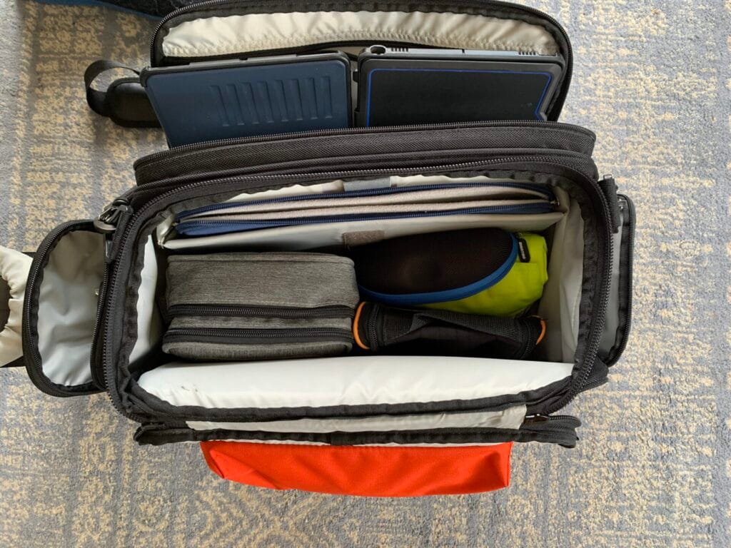 A top down view of the Aerocoast Pro Crew I flight bag showing the main compartment packed with a cable bag, headset and various sundries and also the front pocket with two iPads.